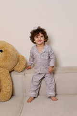 Child in pajamas standing next to a large teddy bear on a couch.