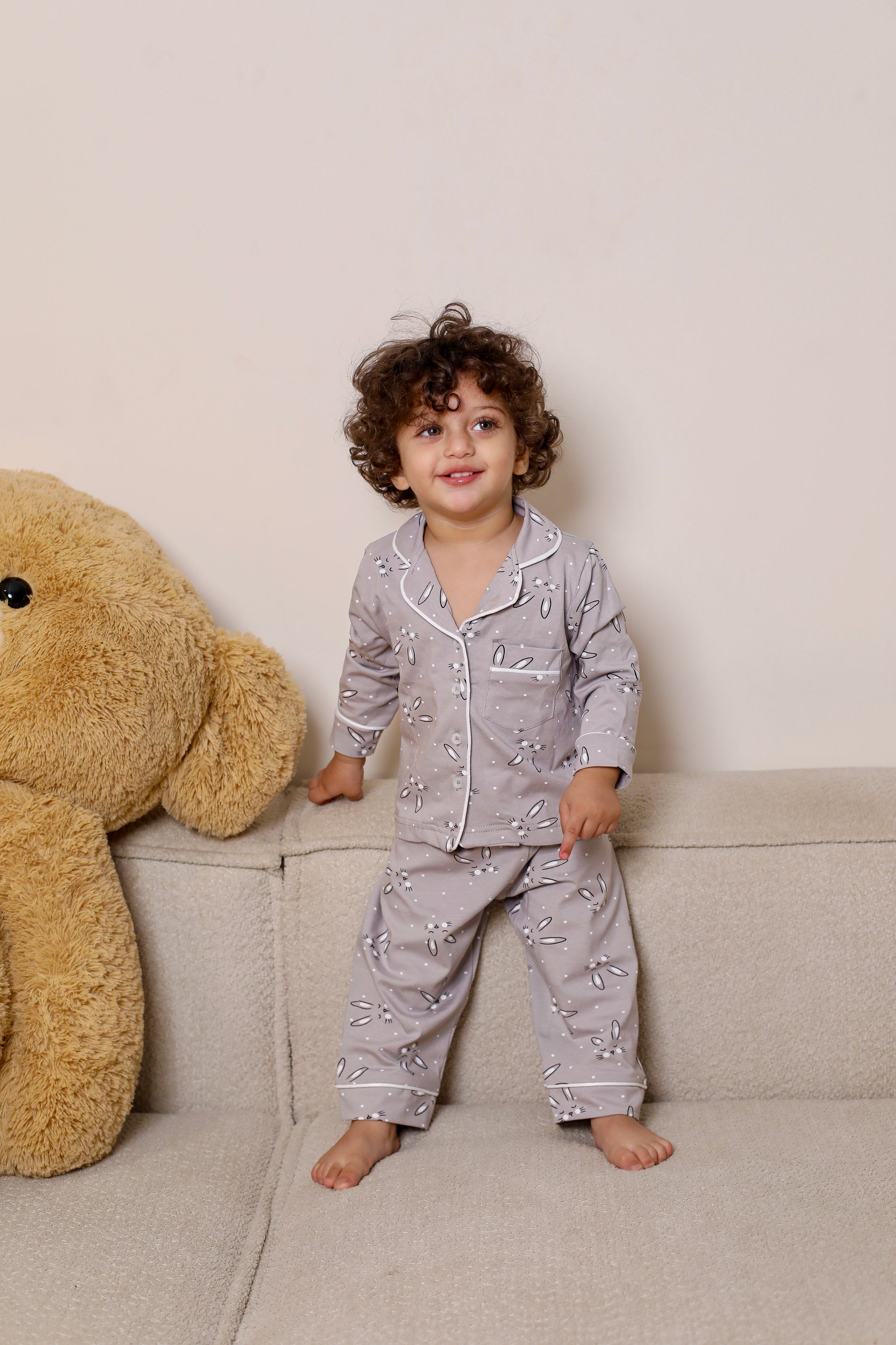 Child in pajamas standing next to a large teddy bear on a couch.