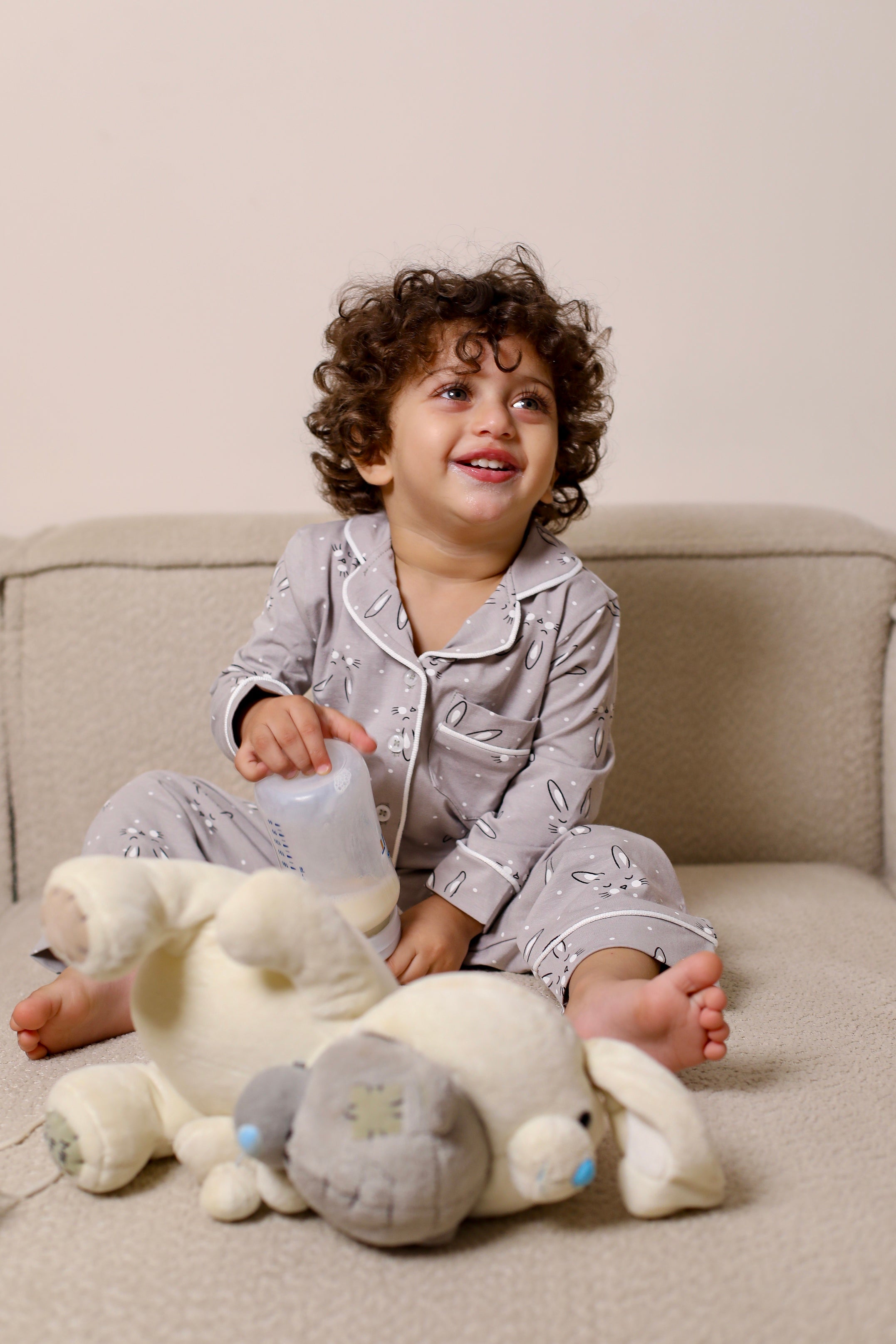 Child in pajamas sitting on a couch with a large teddy bear
