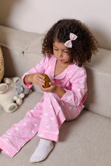 Child in pink pajamas sitting on a couch holding a small object.
