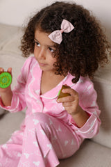 Child in pink pajamas with a bow, holding colorful objects on a light background