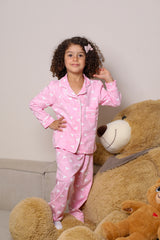 Child in pink pajamas with heart patterns sitting on a large teddy bear against a beige background