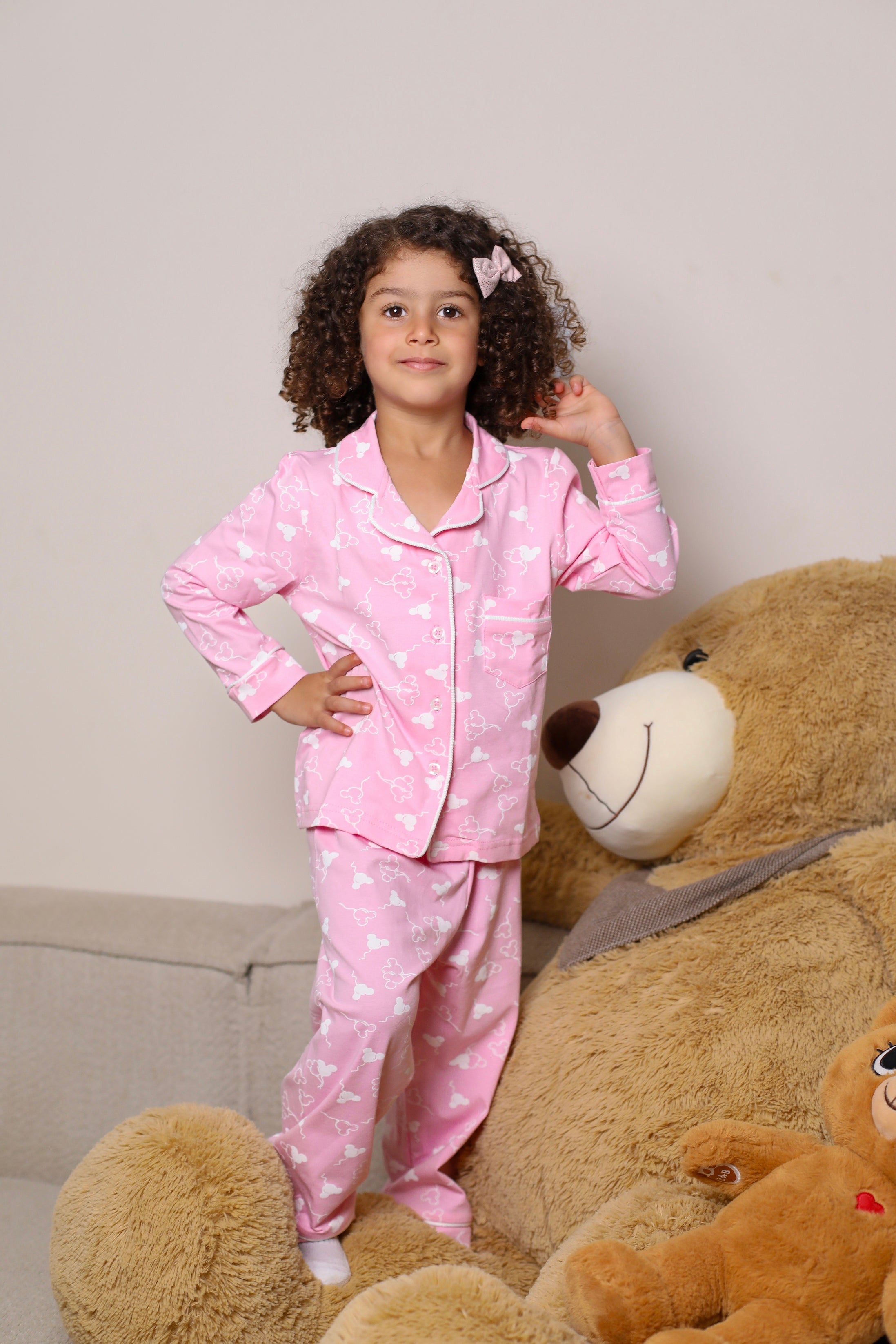 Child in pink pajamas with heart patterns sitting on a large teddy bear against a beige background