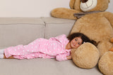 Child in pink pajamas lying on a couch next to a large teddy bear