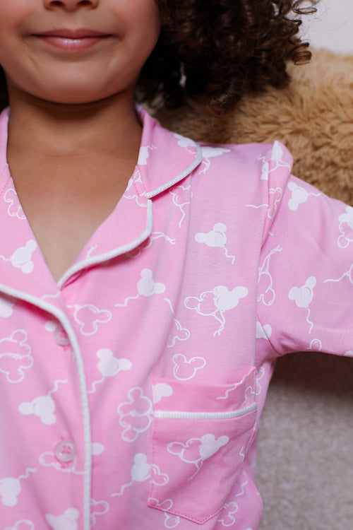 Child wearing pink pajamas with white patterns, sitting on a brown surface.